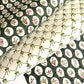 a sheet of block printed paper with a dark green backdrop and white oval scallops with winter foliage motif in the centre.  Pictured with a different design paper with a design of green bows on white