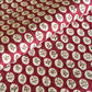 A close-up of a hand block printed paper with a repeating pattern of cream medallions featuring green leaves and red berries on a deep red background.