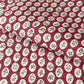 A close-up of a hand block printed paper with a repeating pattern of cream medallions featuring green leaves and red berries on a deep red background.