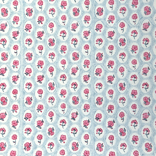 a sheet of hand block printed wrapping paper with a ditsy floral pattern of pink flowers in white ovals with a soft blue backdrop