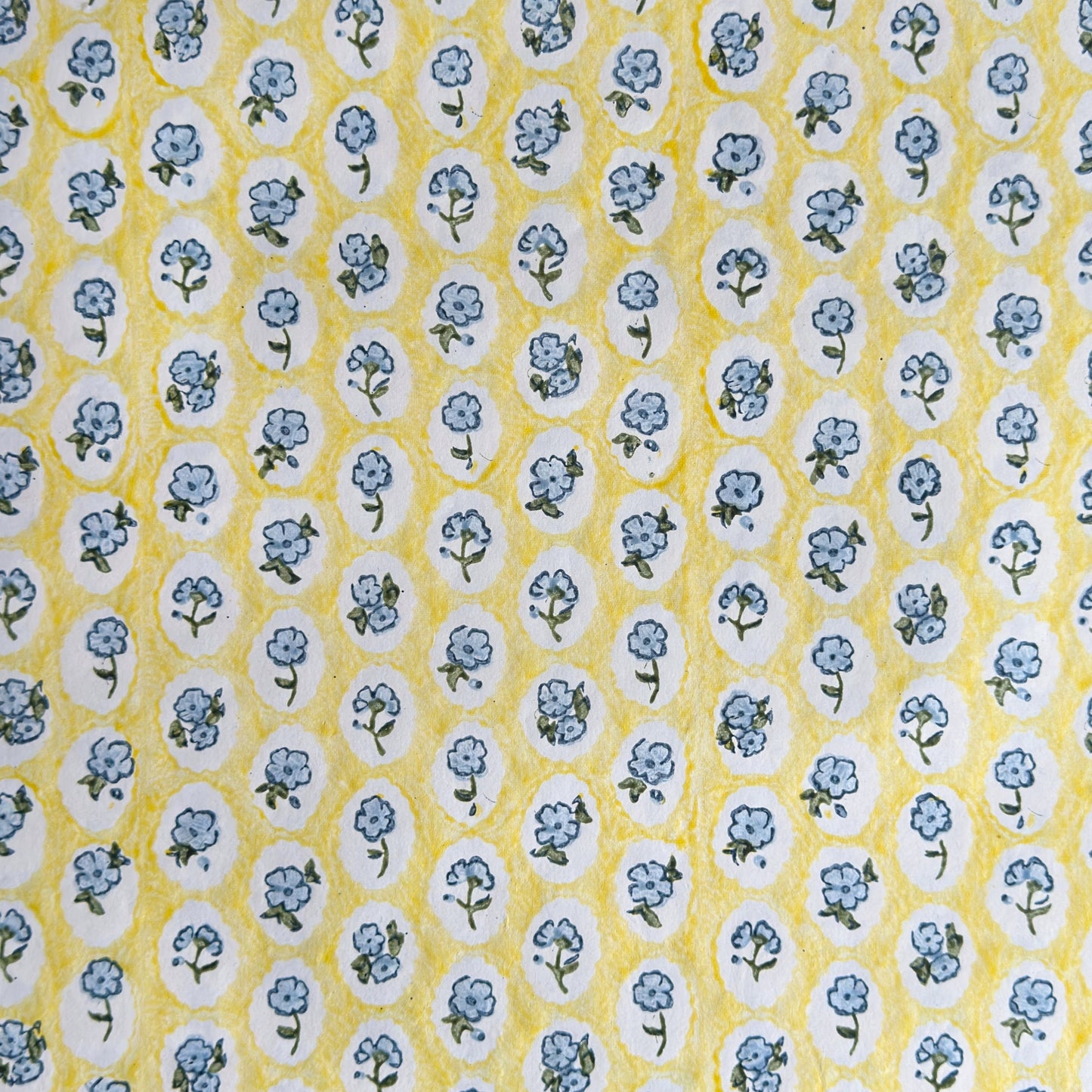 a sheet of hand block printed wrapping paper with a ditsy floral pattern of blue flowers in white ovals with a soft yellow backdrop  