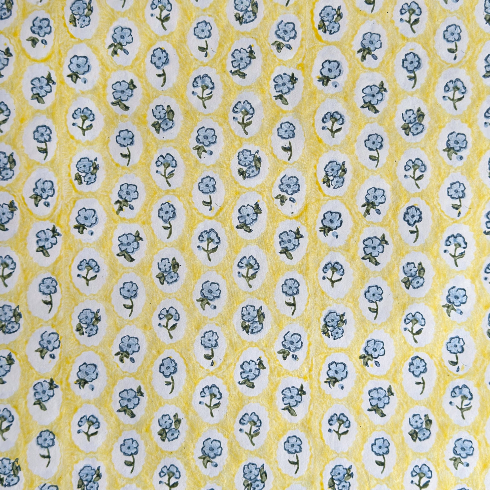 a sheet of hand block printed wrapping paper with a ditsy floral pattern of blue flowers in white ovals with a soft yellow backdrop  