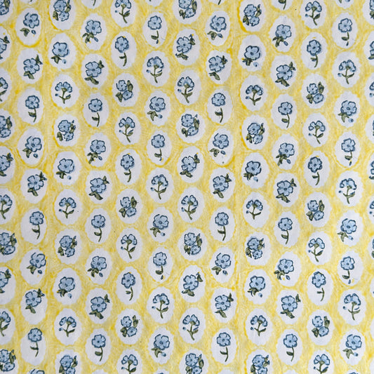 a sheet of hand block printed wrapping paper with a ditsy floral pattern of blue flowers in white ovals with a soft yellow backdrop  