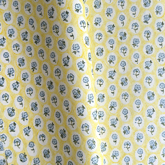 a sheet of hand block printed wrapping paper with a ditsy floral pattern of blue flowers in white ovals with a soft yellow backdrop  