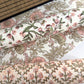a sheet of hand-block printed wrapping paper with a pattern of a songbird amongst flowering branches in blush pink, soft green and gold. Pictured rolled with other designs