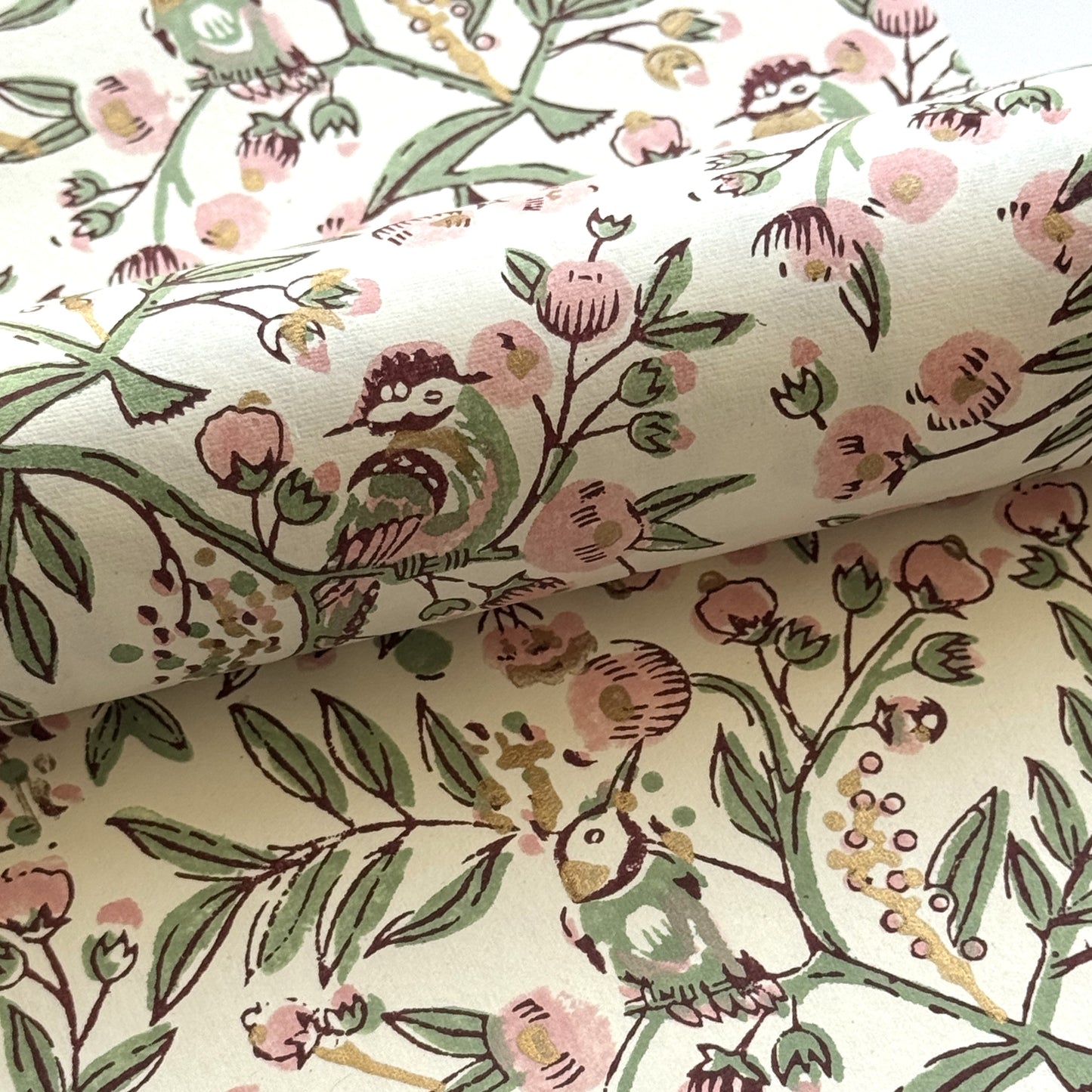 a sheet of hand-block printed wrapping paper with a pattern of a songbird amongst flowering branches in blush pink, soft green and gold