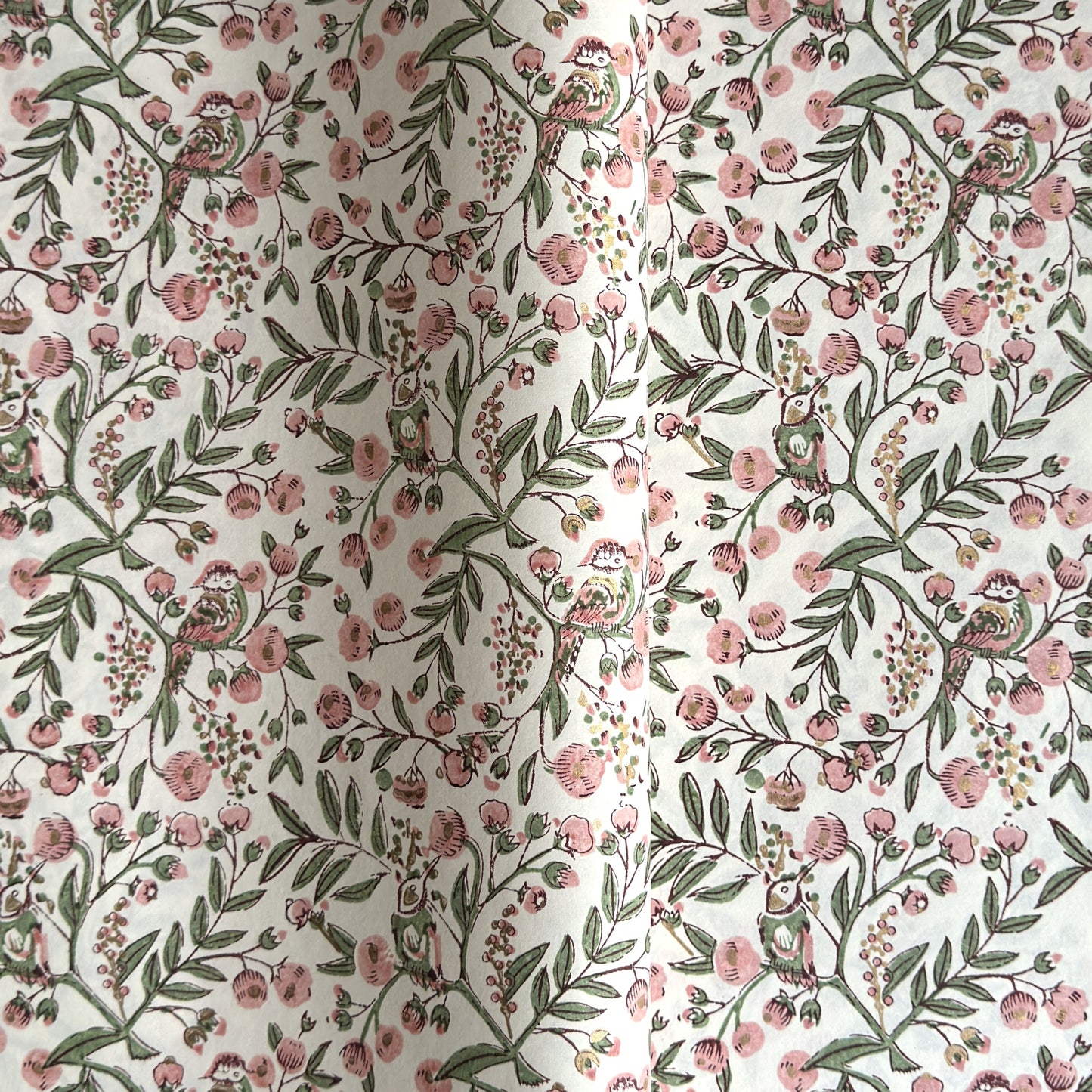 a sheet of hand-block printed wrapping paper with a pattern of a songbird amongst flowering branches in blush pink, soft green and gold