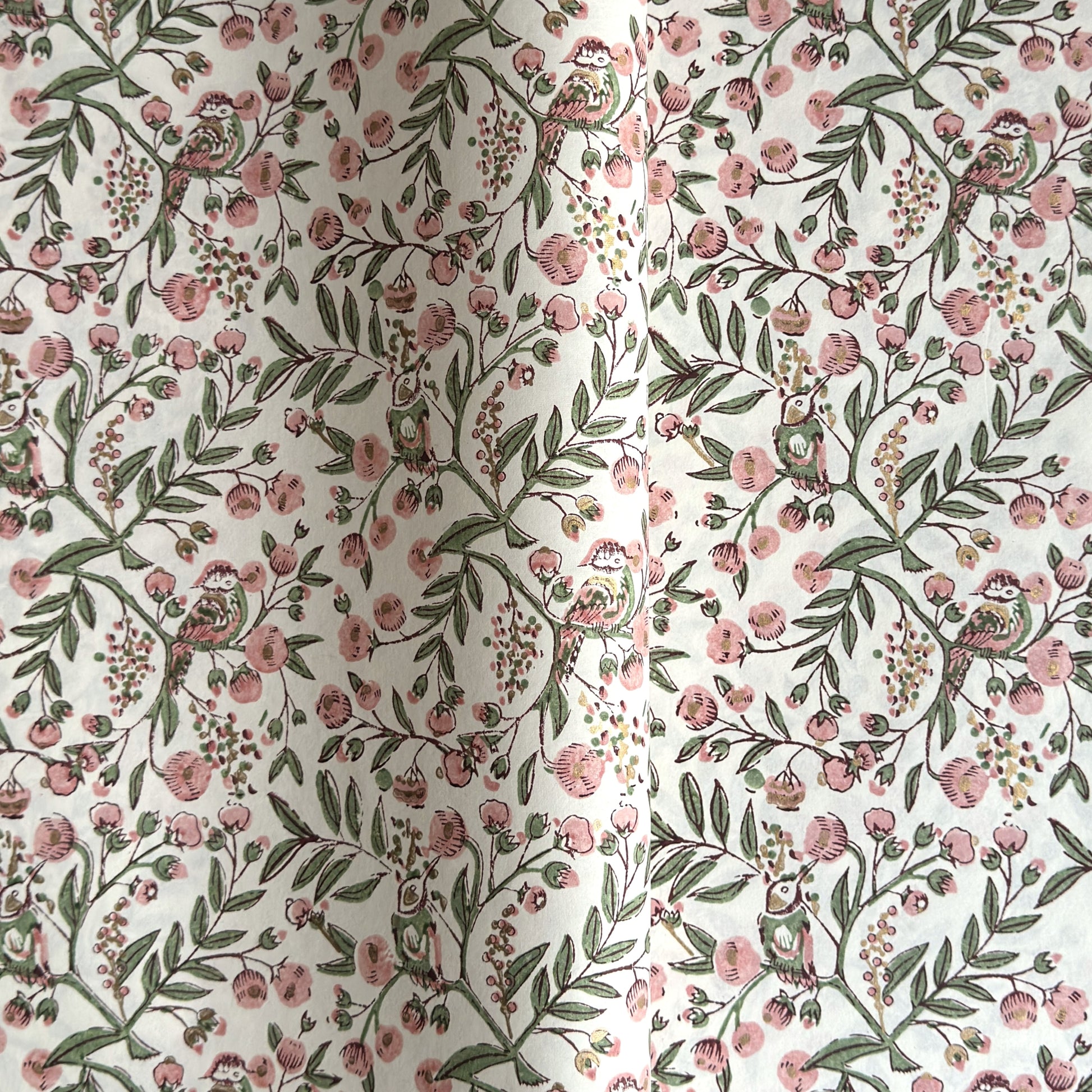 a sheet of hand-block printed wrapping paper with a pattern of a songbird amongst flowering branches in blush pink, soft green and gold