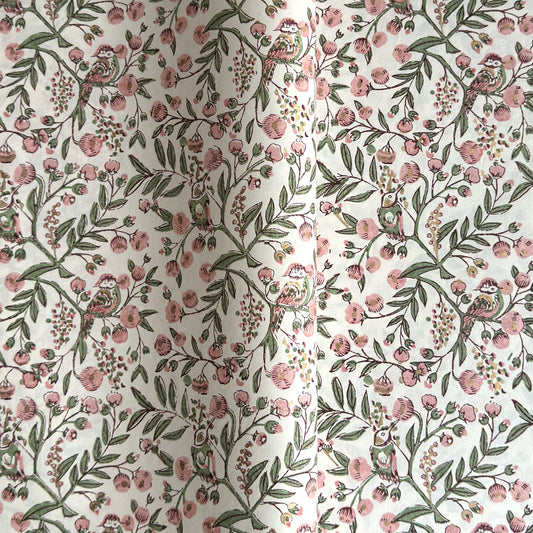 a sheet of hand-block printed wrapping paper with a pattern of a songbird amongst flowering branches in blush pink, soft green and gold