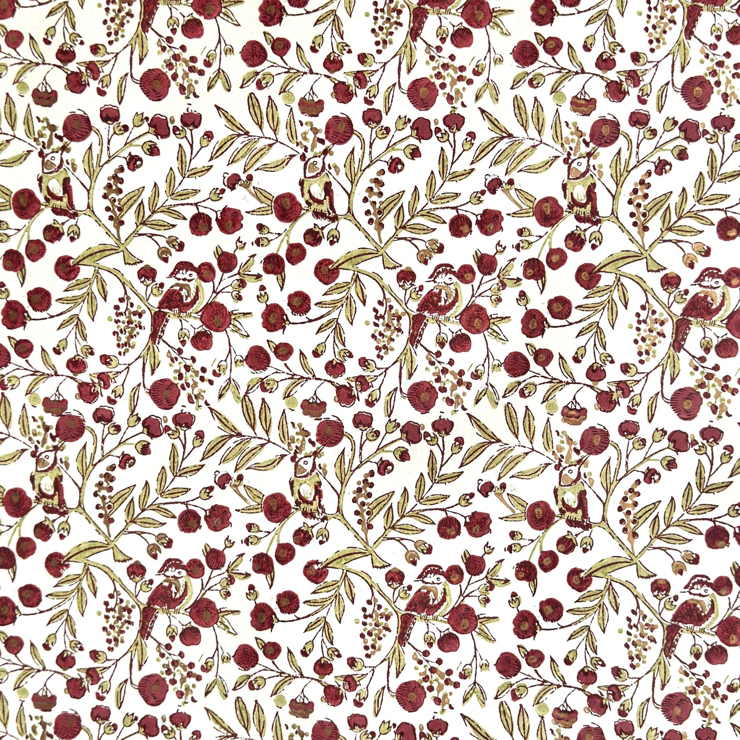 a sheet of hand block printed paper with a repeat pattern of foliage, flowers and a songbird in red, green and gold  