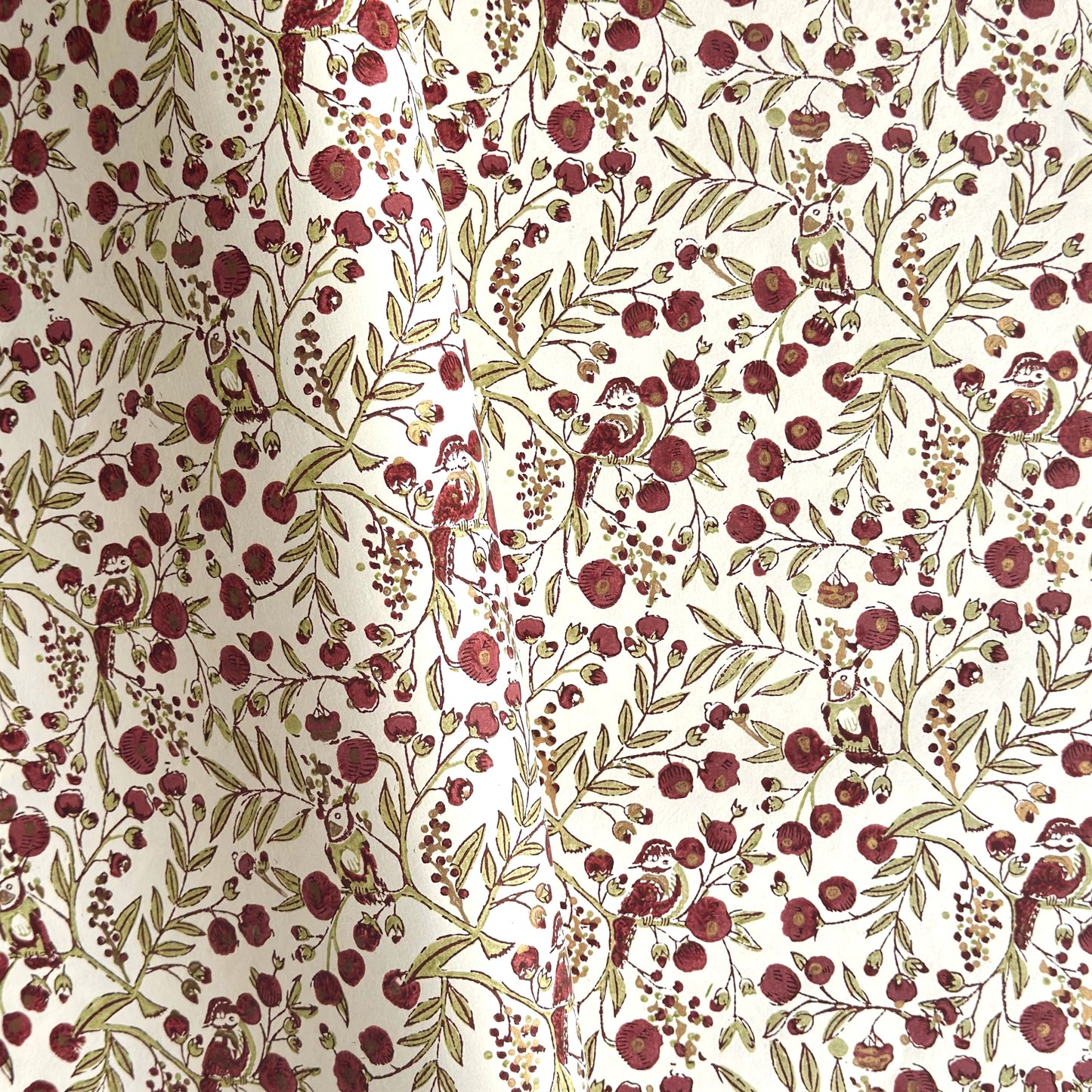 a sheet of hand block printed paper with a repeat pattern of foliage, flowers and a songbird in red, green and gold  