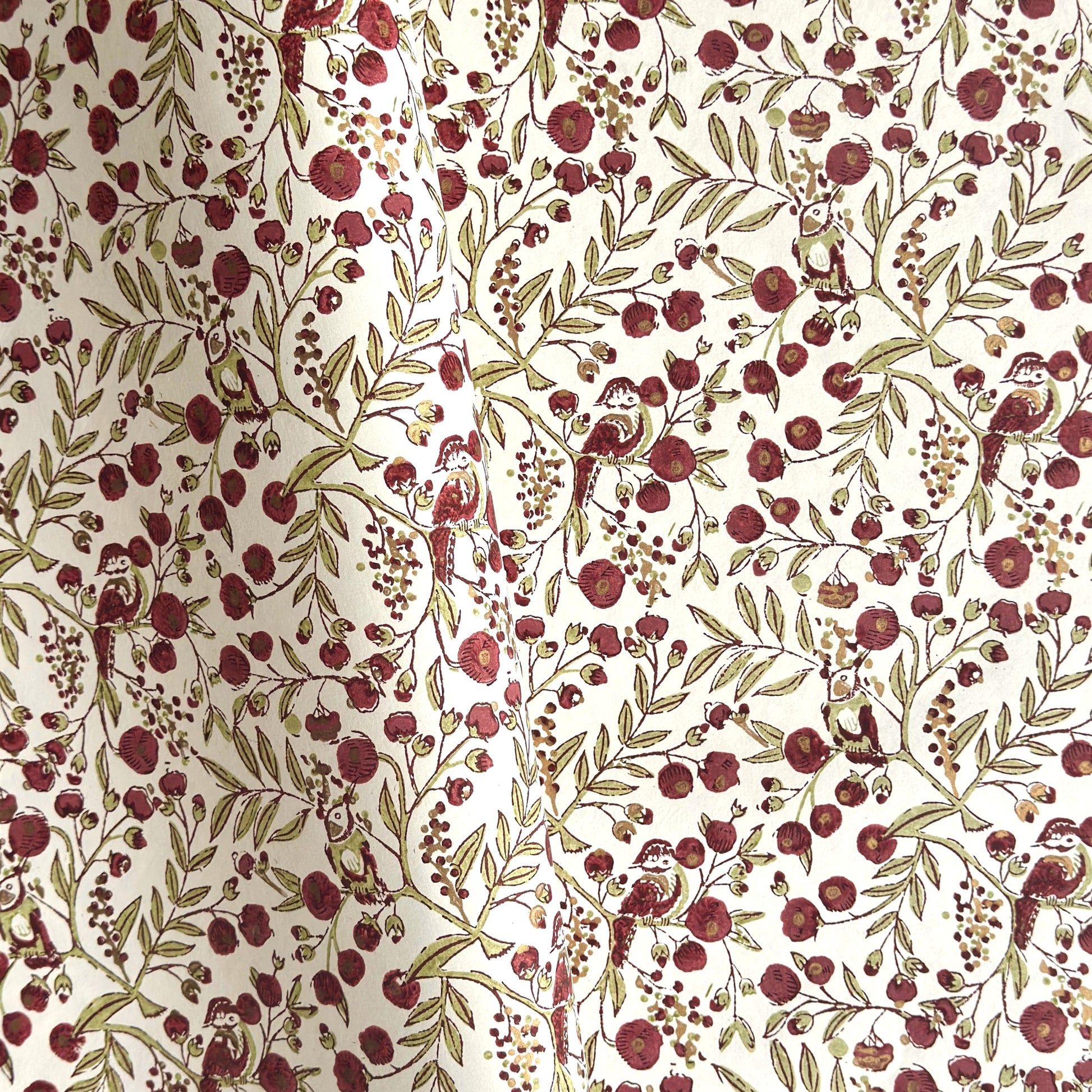 a sheet of hand block printed paper with a repeat pattern of foliage, flowers and a songbird in red, green and gold  