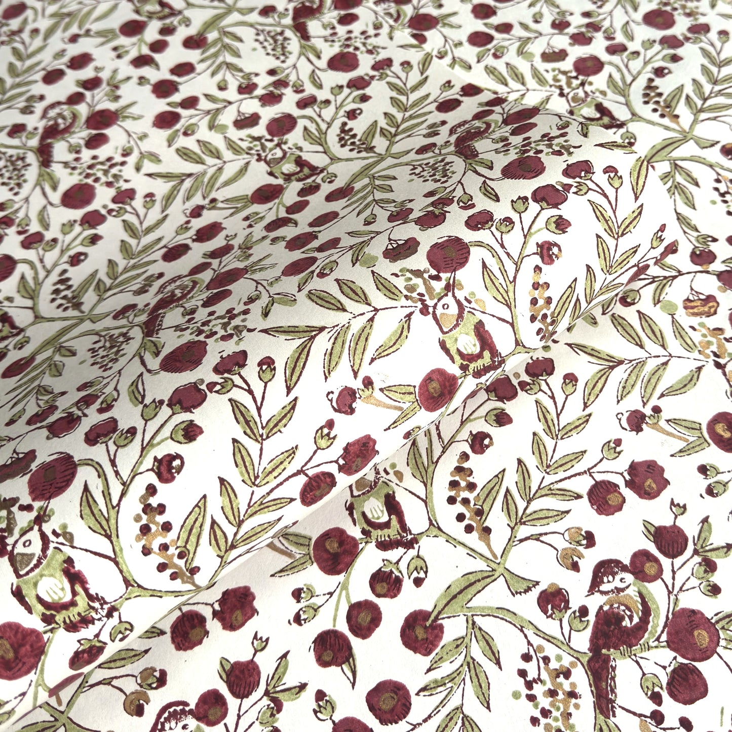 a sheet of hand block printed paper with a repeat pattern of foliage, flowers and a songbird in red, green and gold  