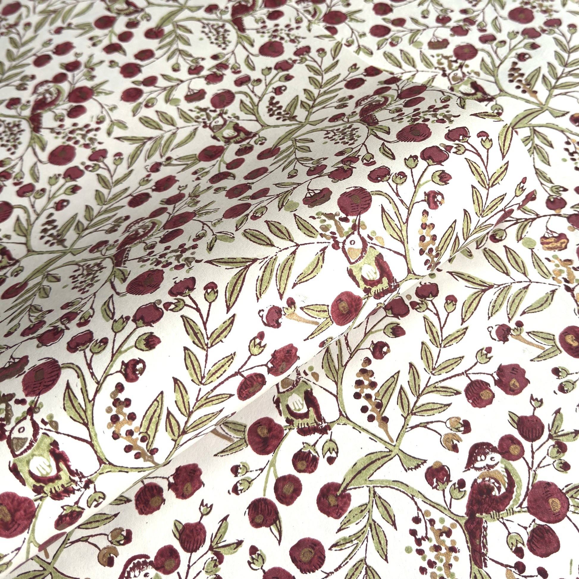 a sheet of hand block printed paper with a repeat pattern of foliage, flowers and a songbird in red, green and gold  