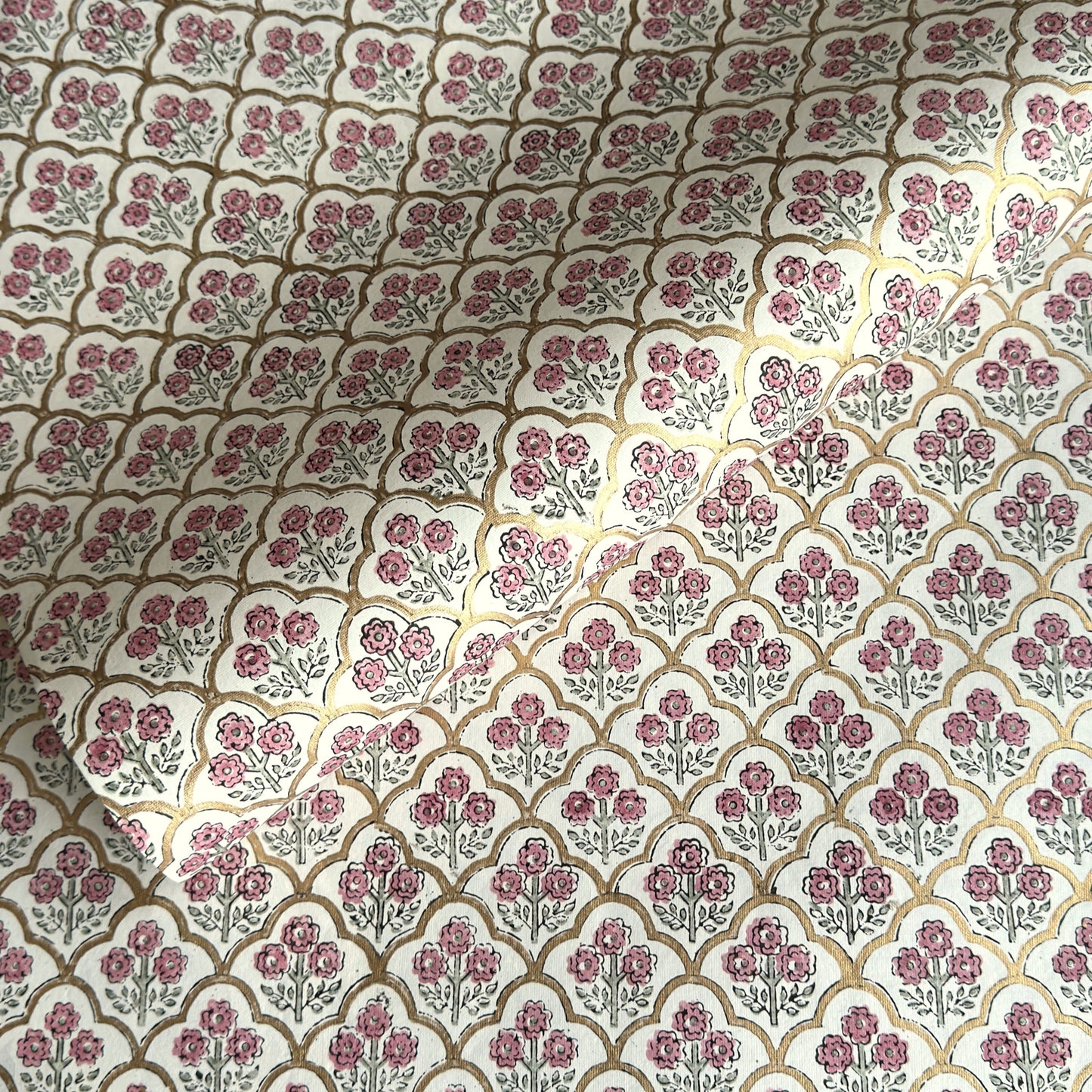 hand block printed wrapping paper by Paper Mirchi.  Repeat pattern of little flowers in pink and green within a gold trellis design.