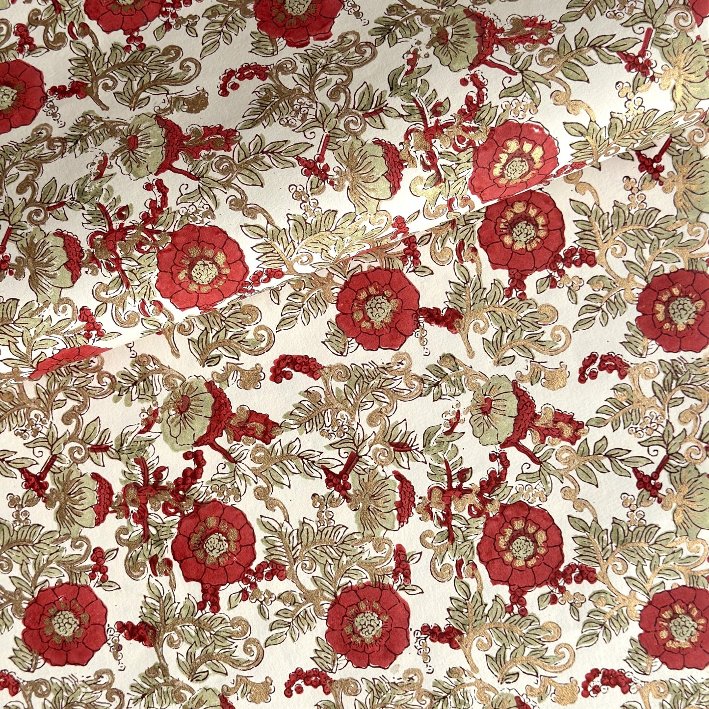 a sheet of hand block printed wrapping paper with a wild rose repeat design in scarlet red with soft green leaves and gold accents