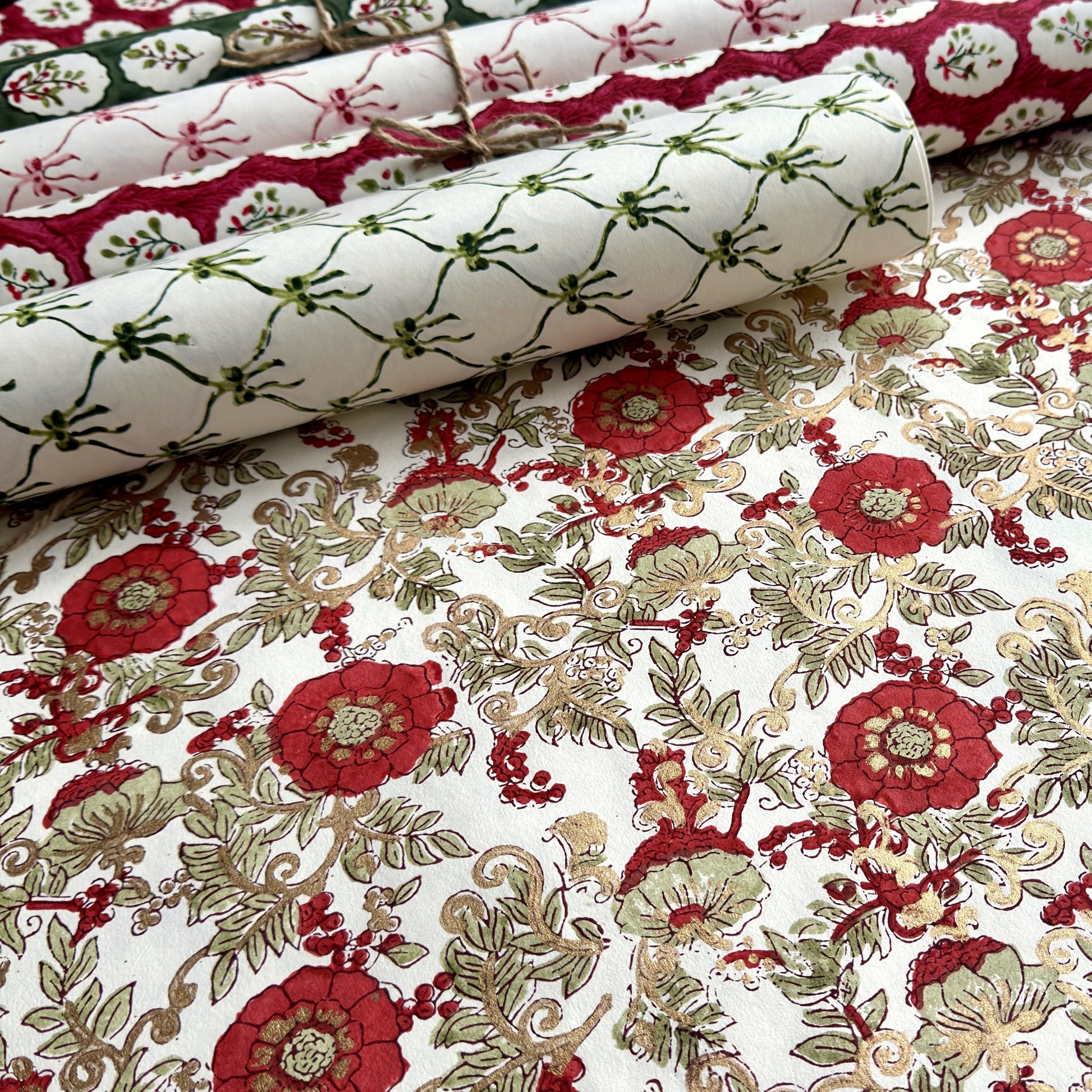 a sheet of hand block printed wrapping paper with a wild rose repeat design in scarlet red with soft green leaves and gold accents