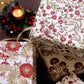 Three gift boxes wrapped in matching floral paper with a vintage botanical pattern, styled with a warm lit candle and red berries in the background.