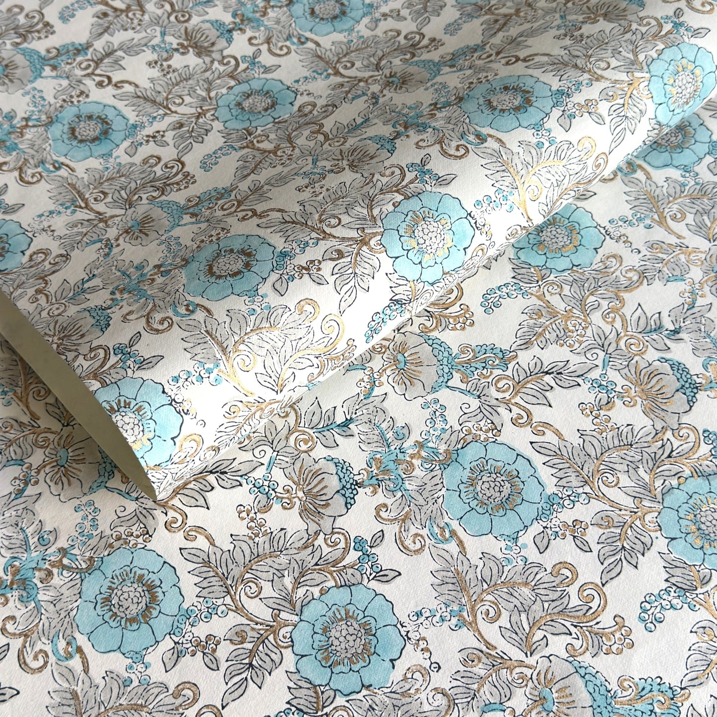 a sheet of hand block printed wrapping paper with a floral wild rose design in opal blue and gold