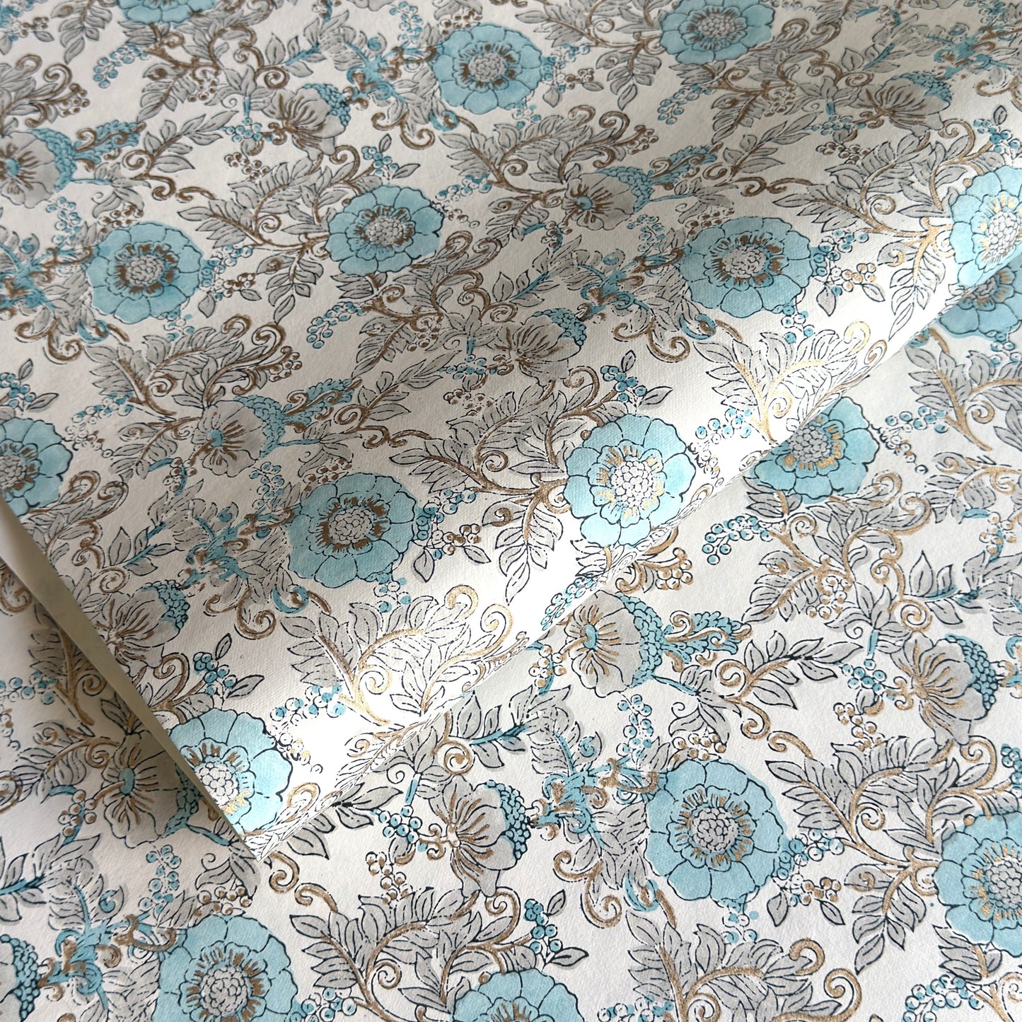 a sheet of hand block printed wrapping paper with a floral wild rose design in opal blue and gold