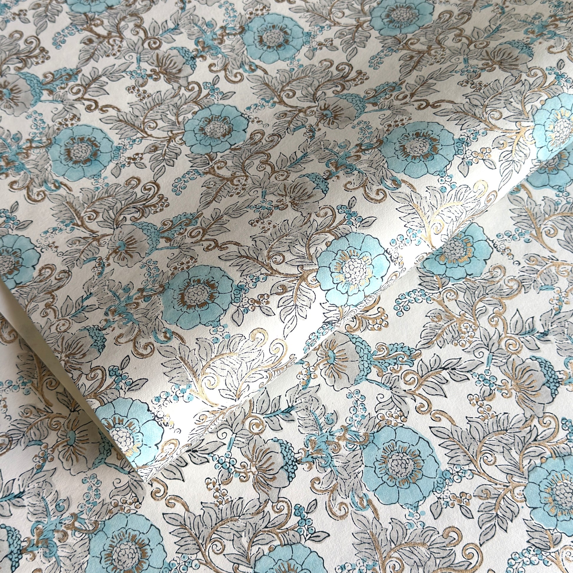 a sheet of hand block printed wrapping paper with a floral wild rose design in opal blue and gold