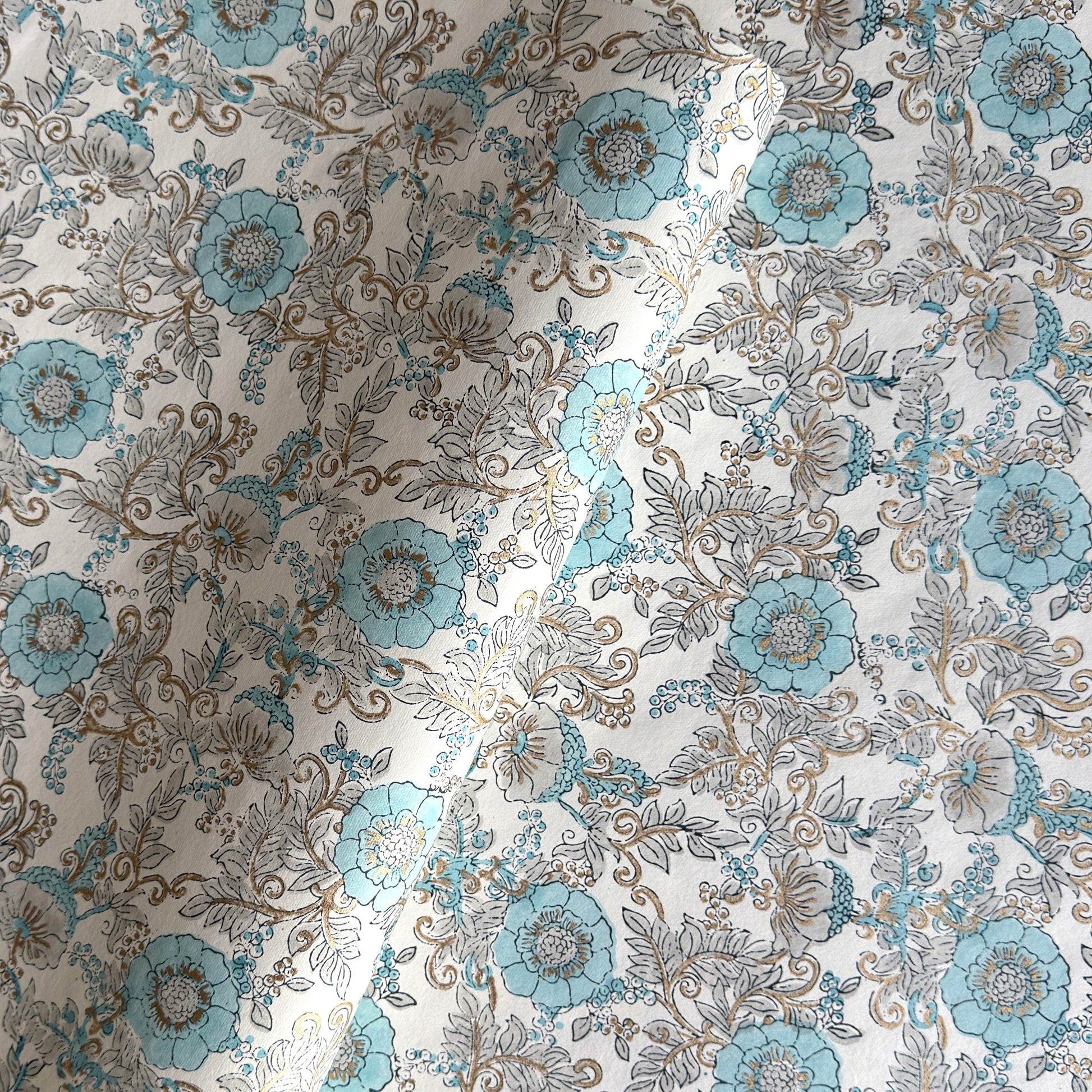 a sheet of hand block printed wrapping paper with a floral wild rose design in opal blue and gold