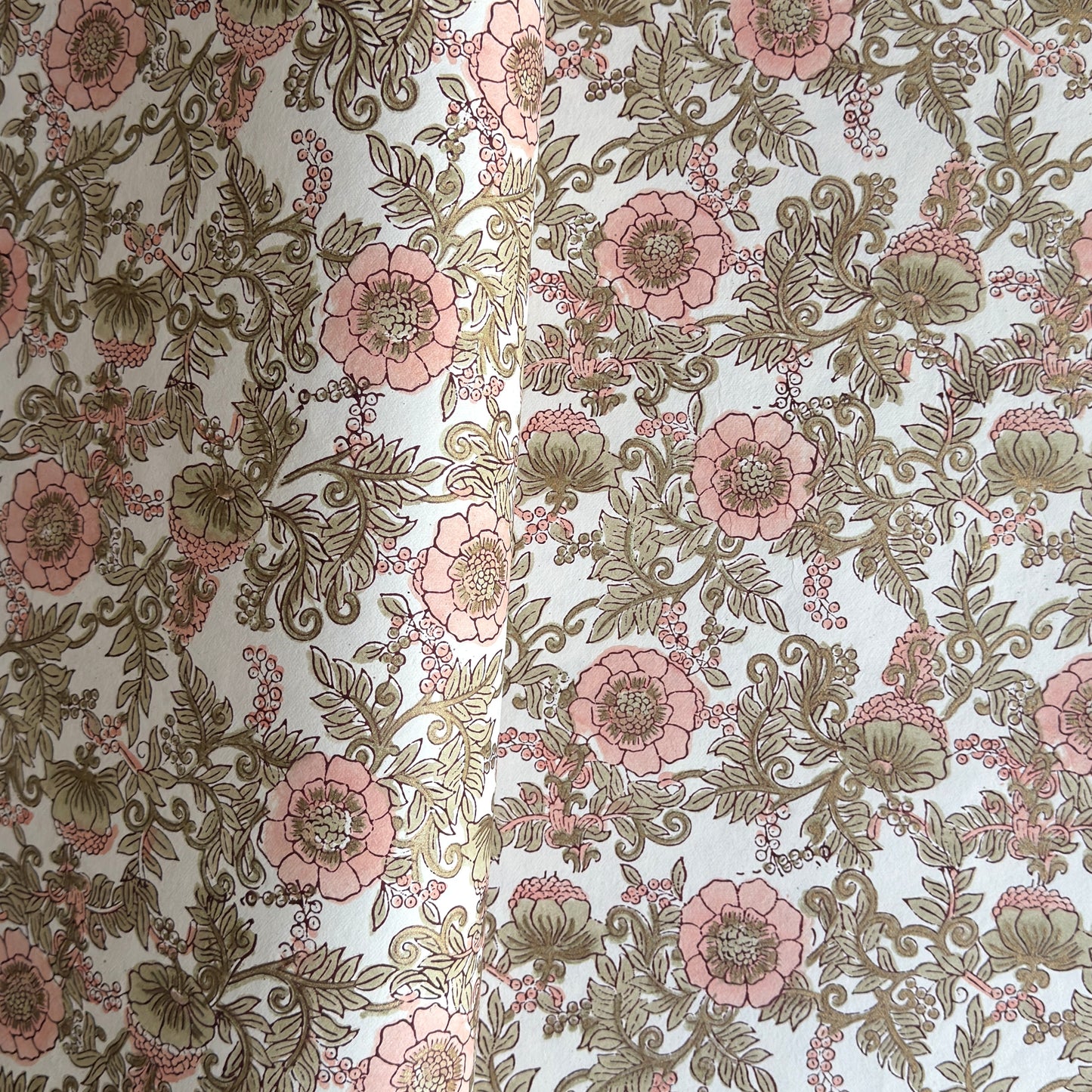 a hand block printed sheet of wrapping paper with a wild rose design in coral, moss green on a white background