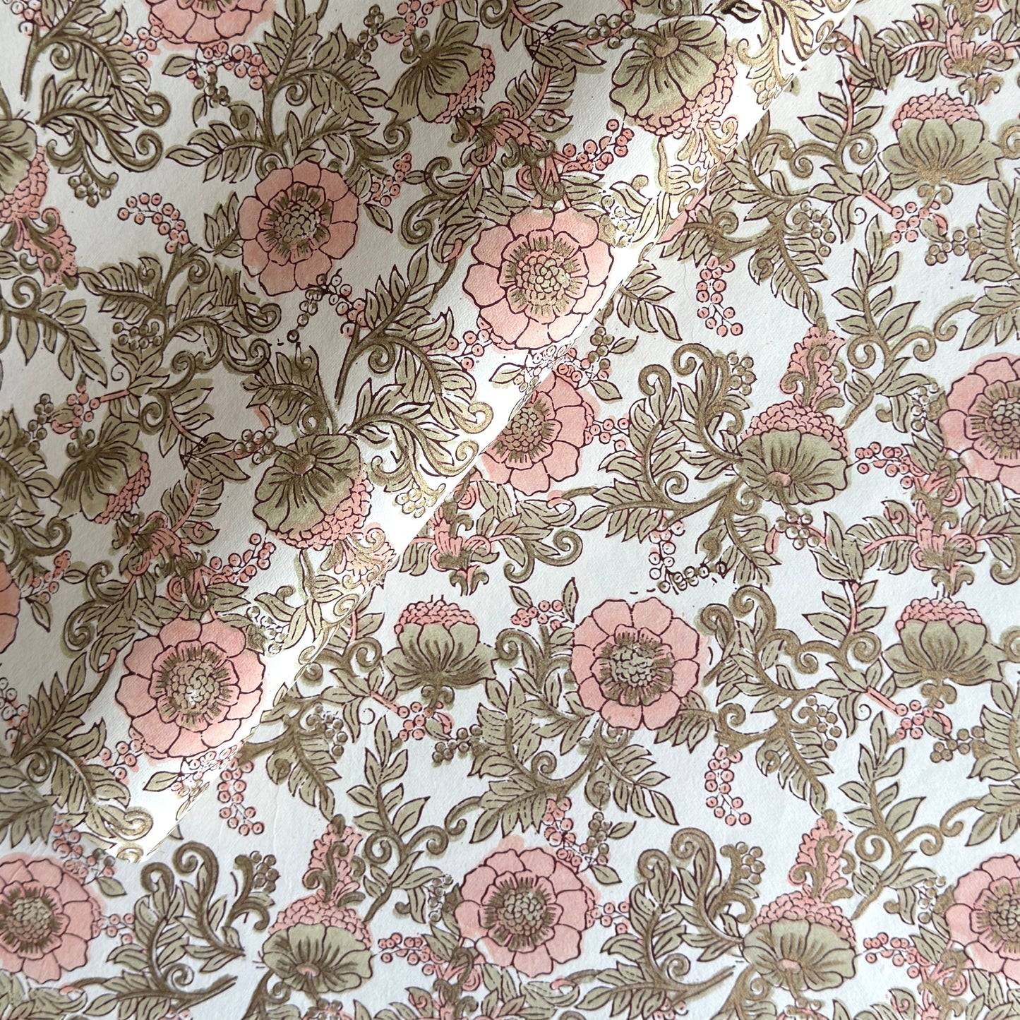 a hand block printed sheet of wrapping paper with a wild rose design in coral, moss green on a white background
