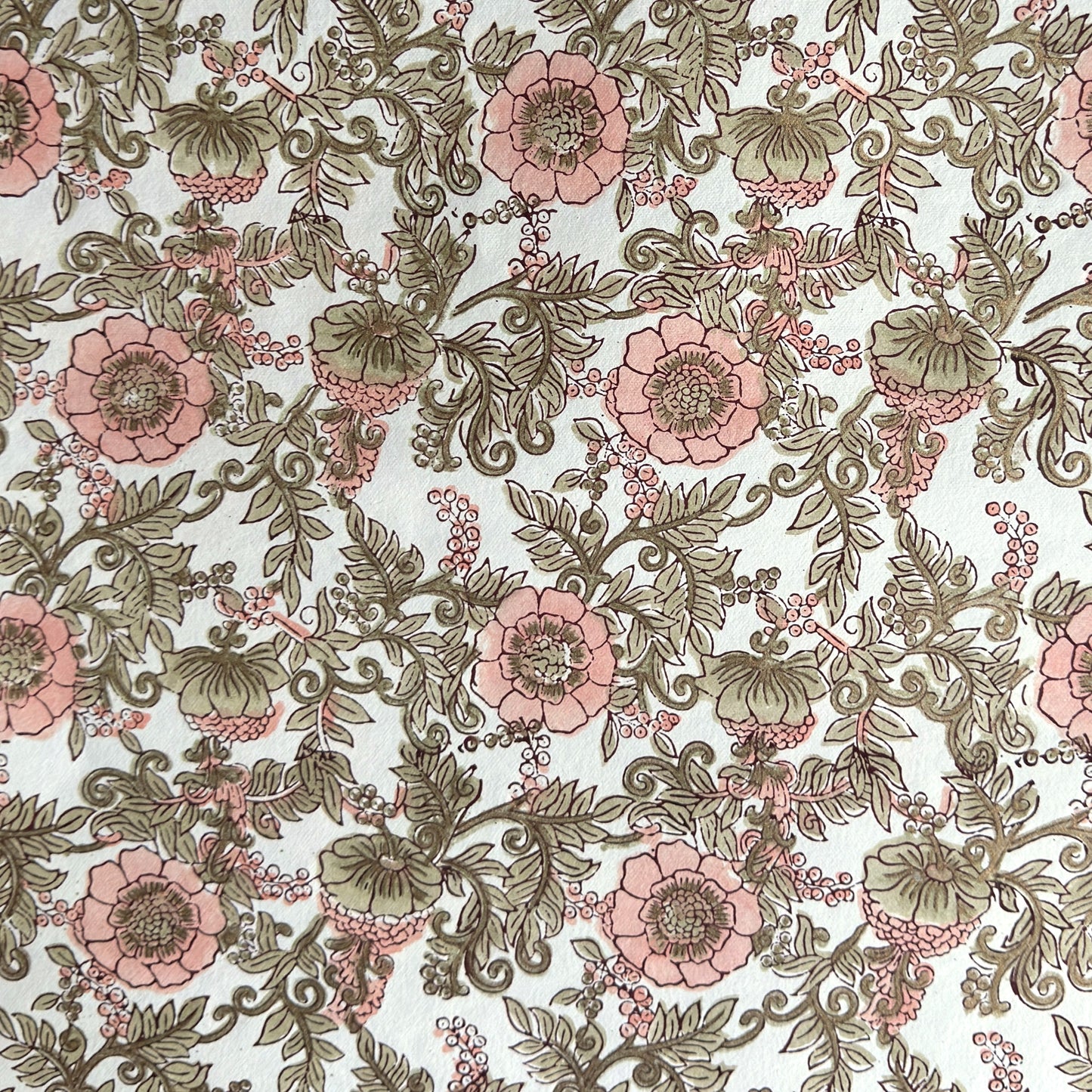 a hand block printed sheet of wrapping paper with a wild rose design in coral, moss green on a white background