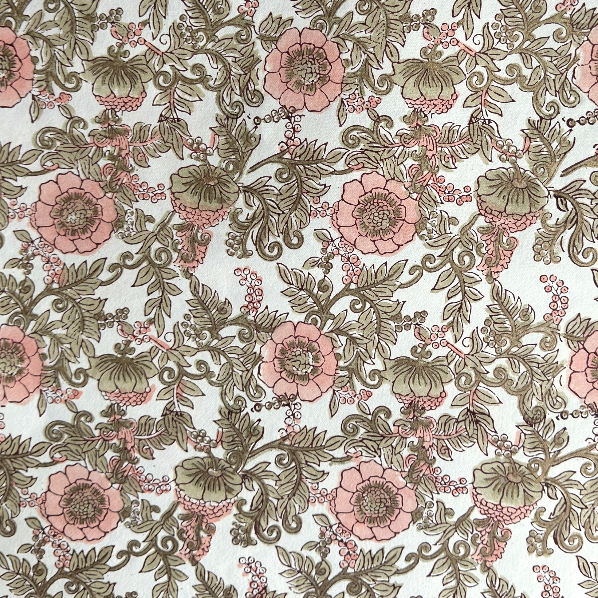 a hand block printed sheet of wrapping paper with a wild rose design in coral, moss green on a white background