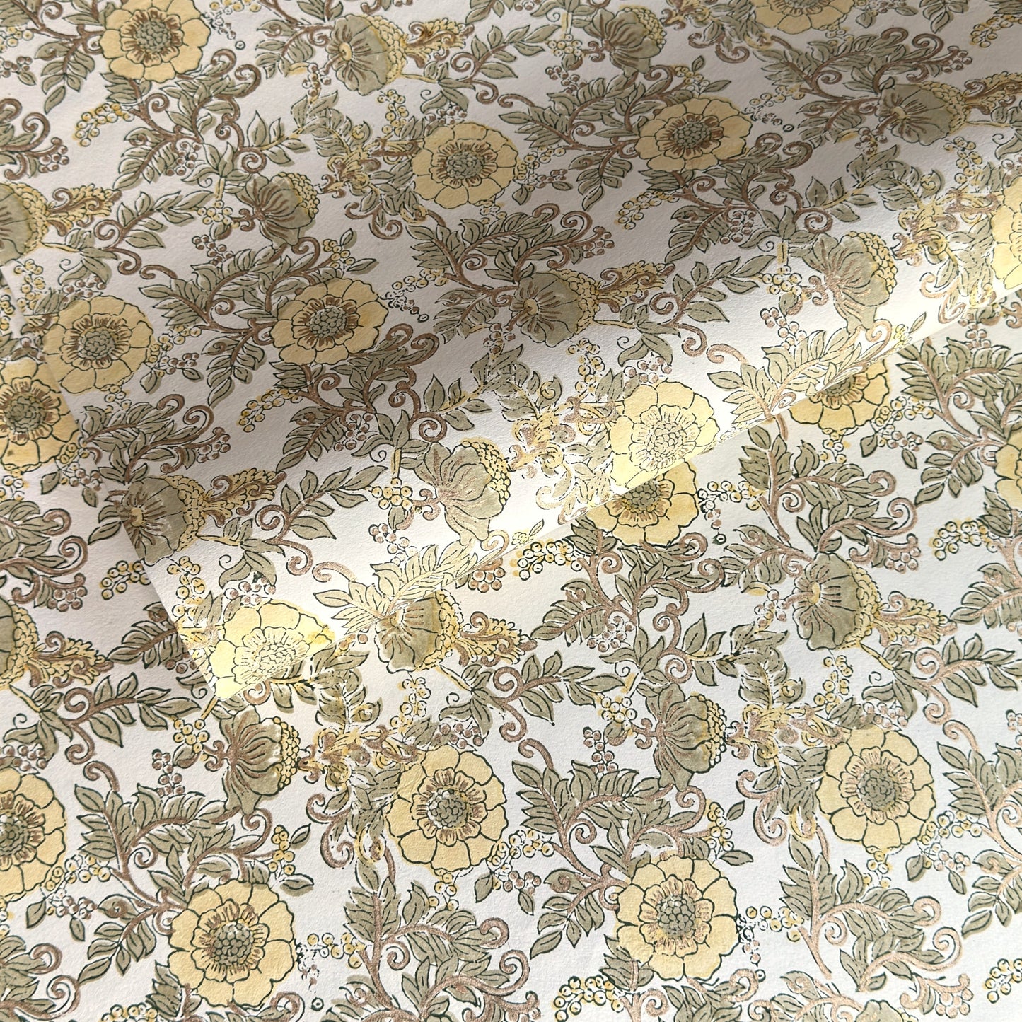 a sheet of hand block printed wrapping paper with a wild rose pattern in buttermilk yellow, moss green and gold