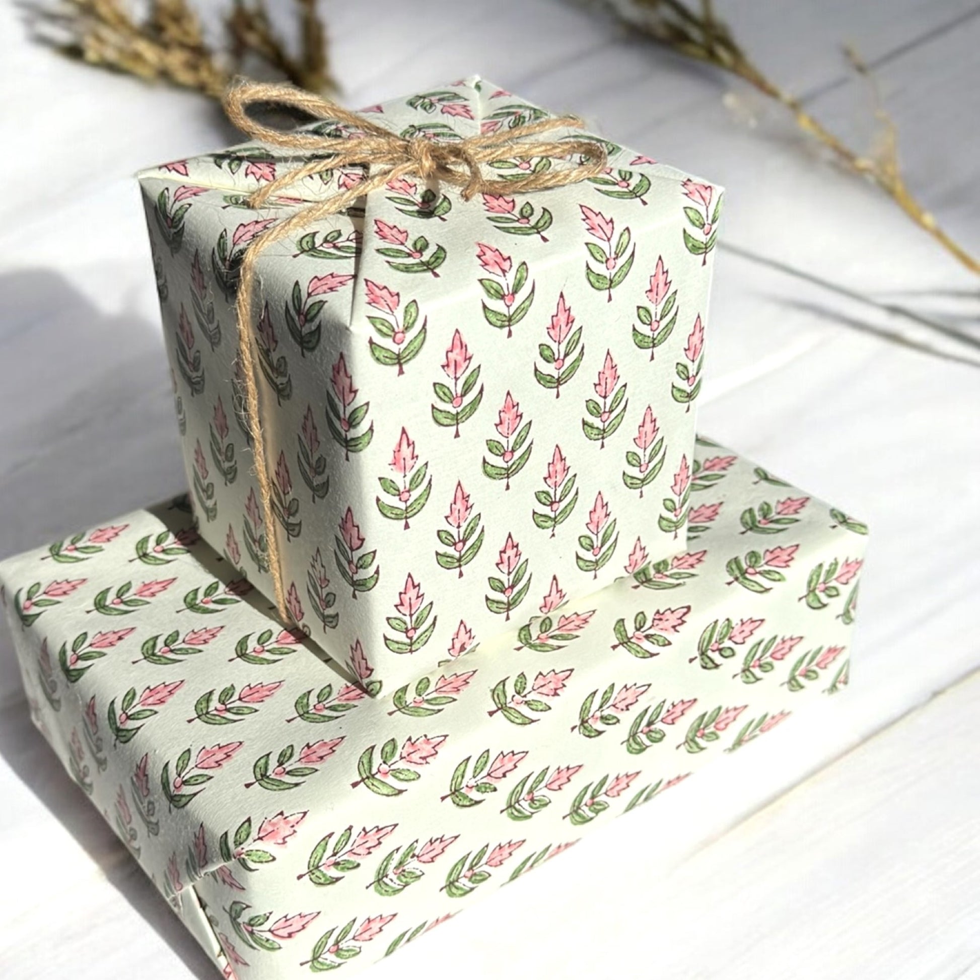 hand block printed paper by Paper Mirchi.  Repeat design of a stylised flower in blush pink and green on a white background. Pictured wrapping two presents and tied with twine