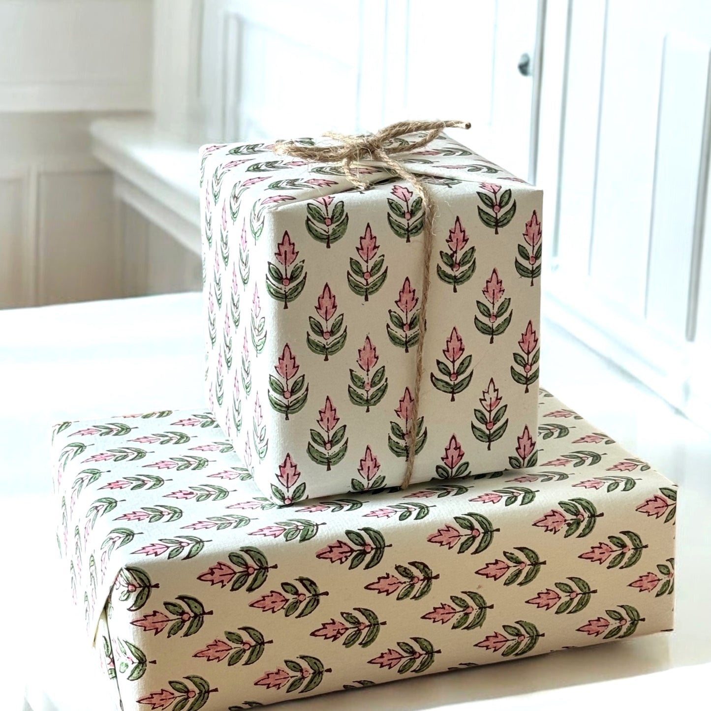 hand block printed paper by Paper Mirchi.  Repeat design of a stylised flower in blush pink and green on a white background.  Pictured wrapping presents