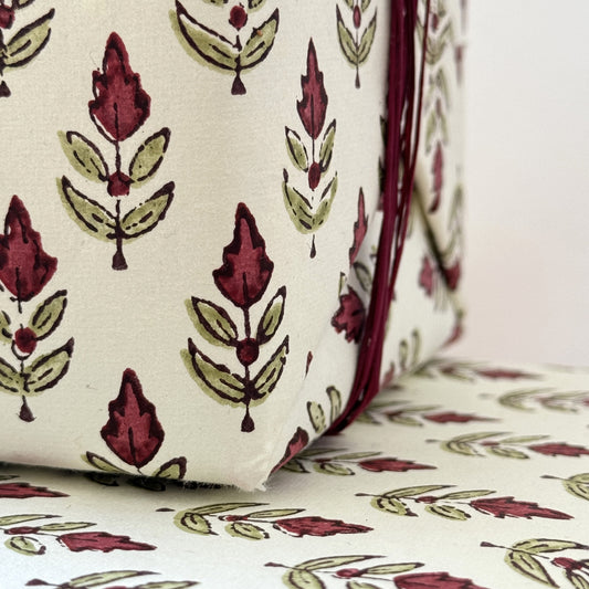 block printed paper by Paper Mirchi with a repeat block print pattern of a little stylised flower in dark burgundy and soft green on white backdrop. Close up