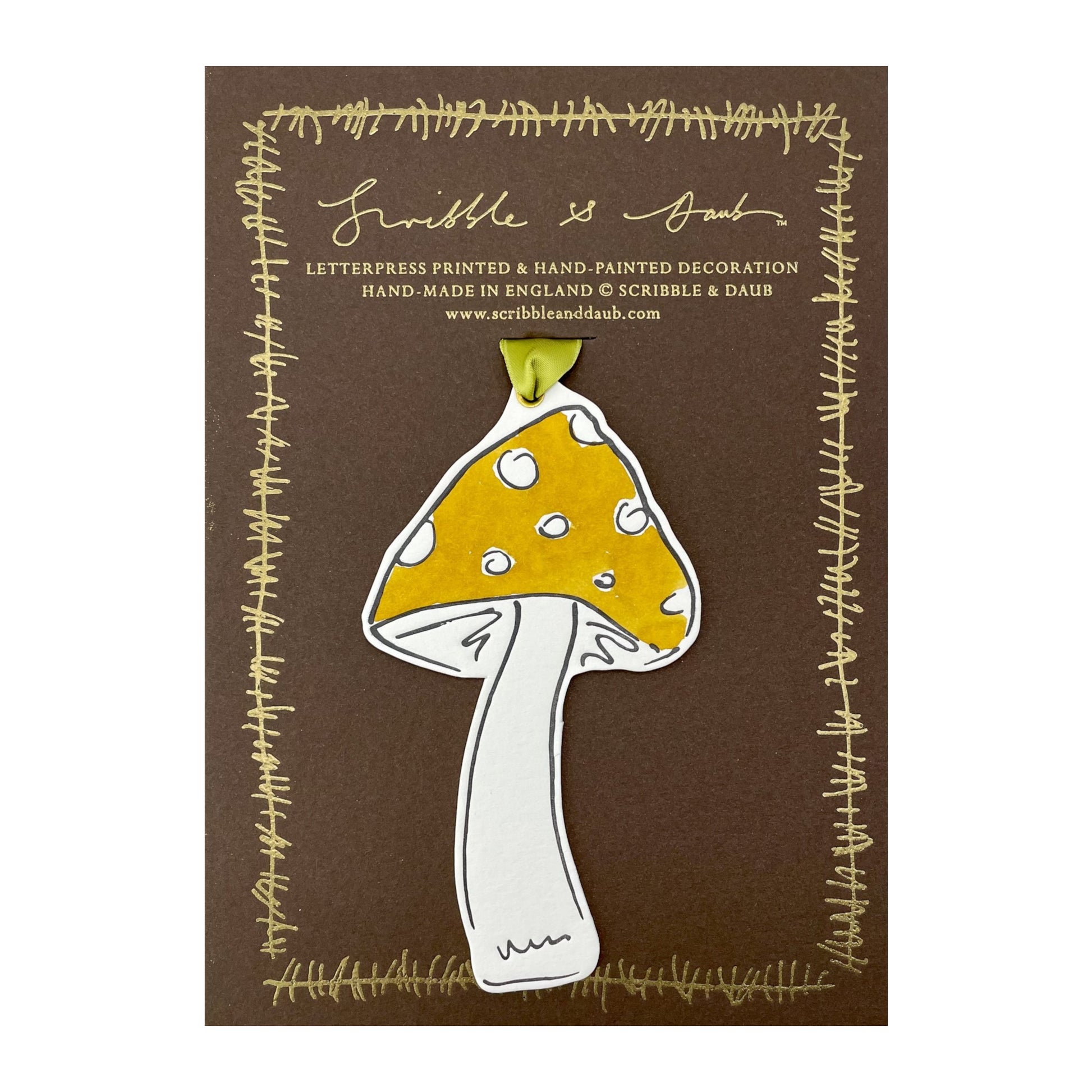 a mushroom shaped hanging ornament made of thick 1050gsm off-white card, letterpress printed in black and then hand painted in ochre ink. It has a chartreuse green satin ribbon to hang the ornament with. By Scribble & Daub. Pictured on a gold-foiled brown board.