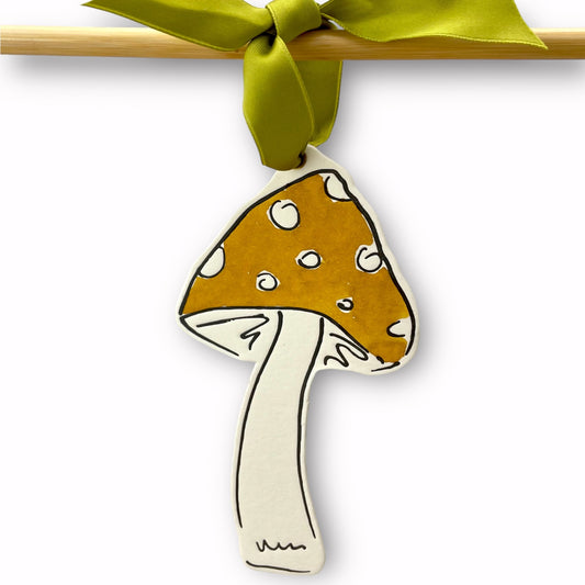 a mushroom shaped hanging ornament made of thick 1050gsm off-white card, letterpress printed in black and then hand painted in ochre ink. It has a chartreuse green satin ribbon to hang the ornament with. By Scribble & Daub.