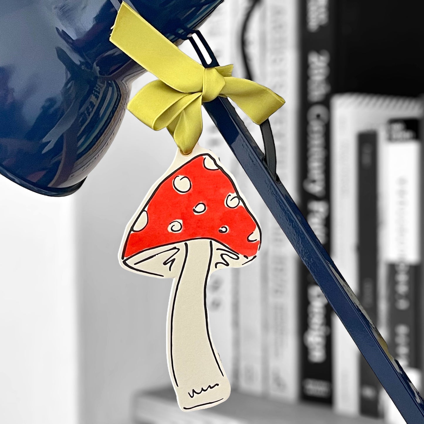 a mushroom shaped hanging ornament made of thick 1050gsm off-white card, letterpress printed in black and then hand painted in red ink. It has a chartreuse green satin ribbon to hang the ornament with. By Scribble & Daub. Pictured hanging from a lamp