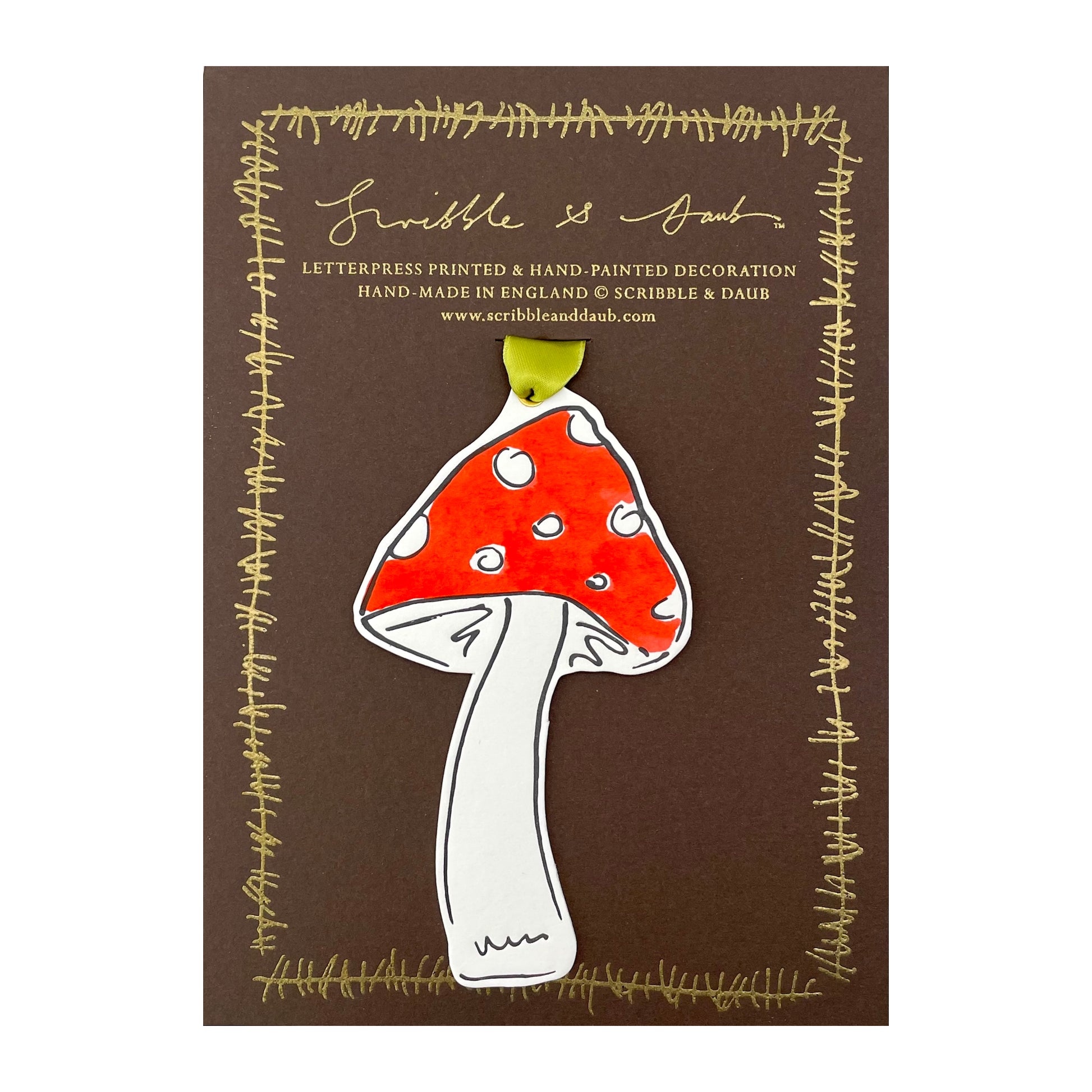 a mushroom shaped hanging ornament made of thick 1050gsm off-white card, letterpress printed in black and then hand painted in red ink. It has a chartreuse green satin ribbon to hang the ornament with. By Scribble & Daub. Pictured on a gold-foiled brown board.