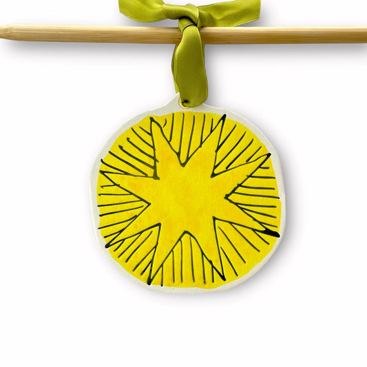 a star shaped hanging ornament made of thick 1050gsm off-white card, letterpress printed in black and then hand painted in yellow ink. It has a chartreuse green satin ribbon to hang the ornament with. By Scribble & Daub. 