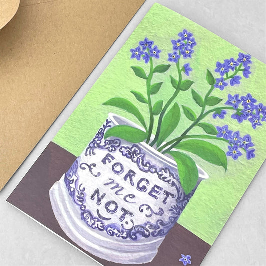 greeting card of a painting of lilac forget-me-nots in a blue and white Staffordshire mug, fresh green backdrop by Susie Hamilton