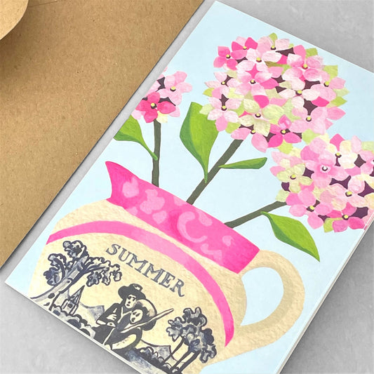 greeting card of a painting of pink hydrangeas in a cream and pink Lustreware jug, pale blue backdrop by Susie Hamilton