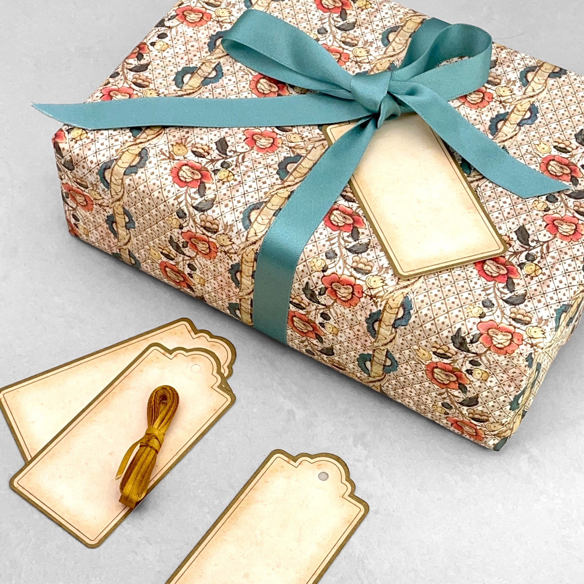 set of 4 vintage style gift tags by Grafiche Tassotti. Rectangular with sepia colour paper and gold border. Presented with gold ribbon.  Pictured with a present wrapped in an Italian patterned paper by Remondini