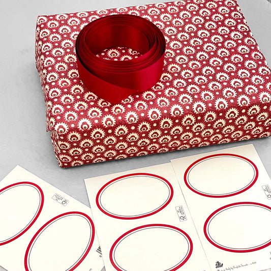 Adhesive labels made of ivory paper with a red oval border by Grafiche Tassotti.  Pictured alongside a wrapped present