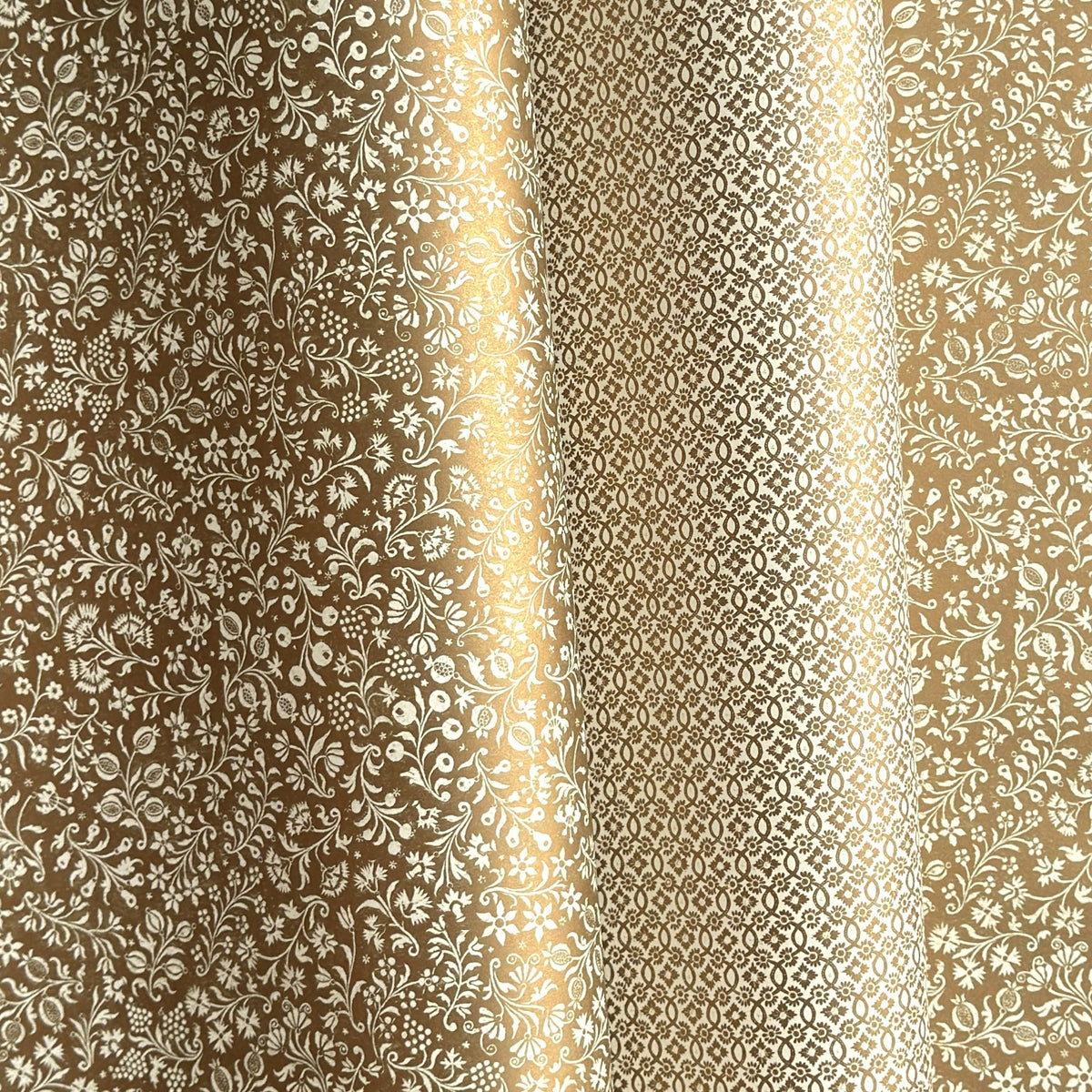 a sheet of Italian wrapping paper by Tassotti, the design is from the Remondini archives and is a small scale botanical block print on an antique gold ground, pictured alongside another paper in with a geometric gold and white pattern