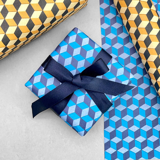 Italian patterned wrapping paper "Carta Varese" by Grafiche Tassotti. A pattern of blue, aqua a navy geometric cubes with a 3D effect. Pictured wrapped as a present with a navy bow