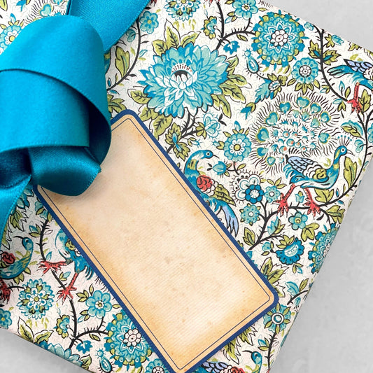 italian patterned wrapping paper "Carta Varese" by Grafiche Tassotti. Pattern of peacocks, flowers and foliage in tones of blue, aqua, green and red. Pictured as a present with ribbon and tag