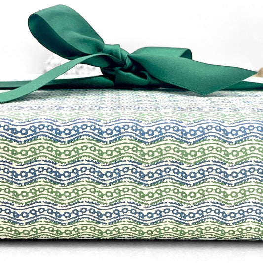italian patterned wrapping paper "Carta Varese" by Grafiche Tassotti. Pattern of small wavy lines in blue and green on a cream backdrop. Pictured with a green ribbon bow