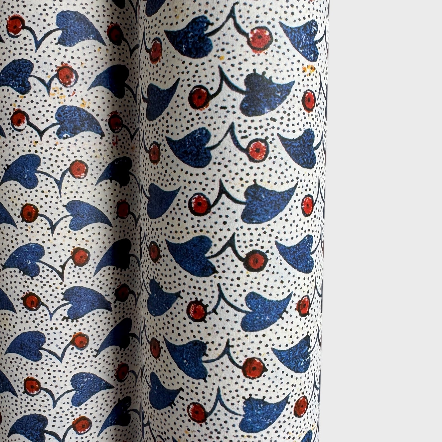 a sheet of italian wrapping paper with a blue little heart shaped leaves and red berries on white background. Close up