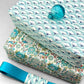 italian Remondini patterned wrapping paper by Tassotti.. All over repeat pattern of block printed style waves in aqua, dark blue on white background.  Pictured wrapped as a present alongside another design