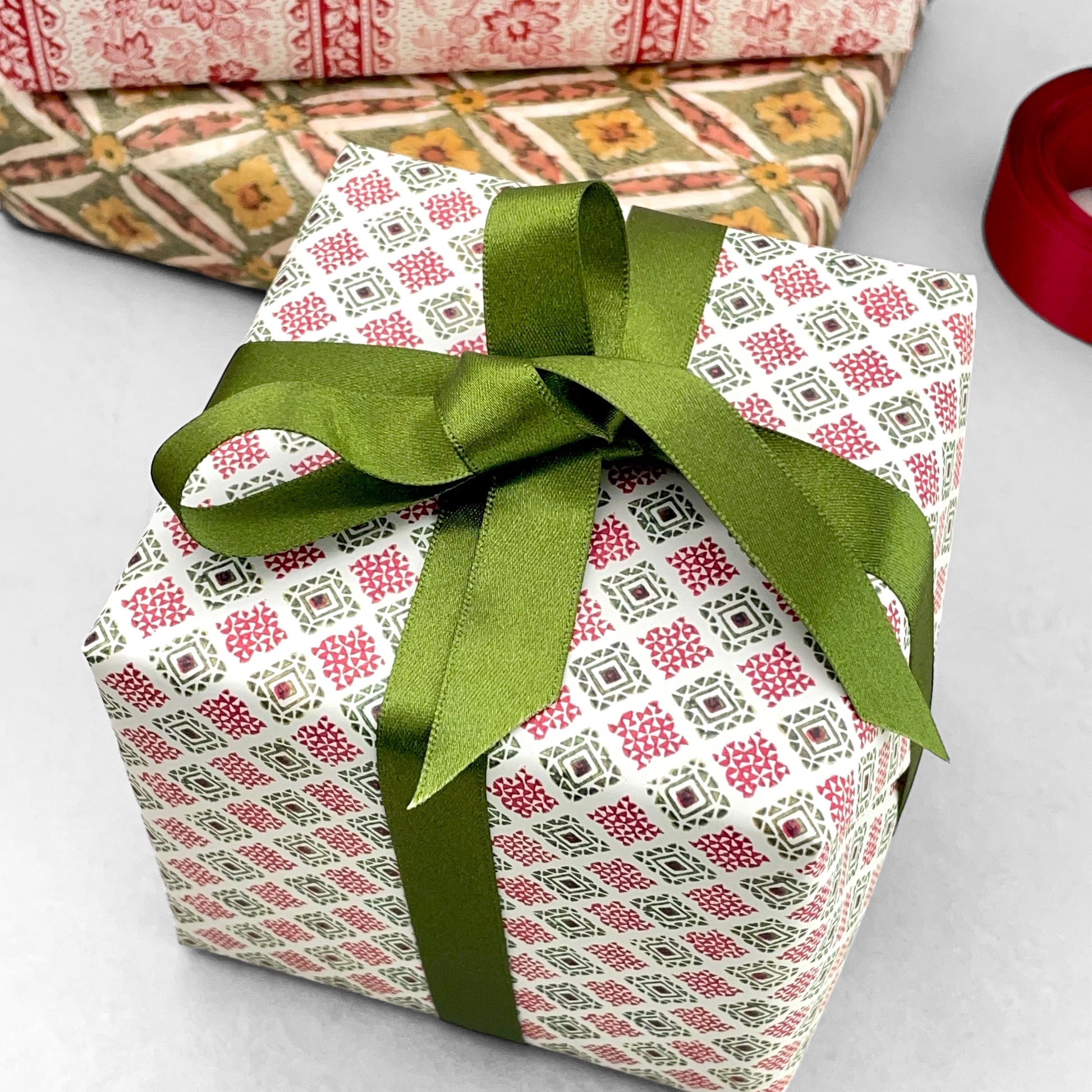 italian Remondini patterned wrapping paper by Tassotti. Block print style red and green diamonds on a white background. Wrapped as a present with a green bow
